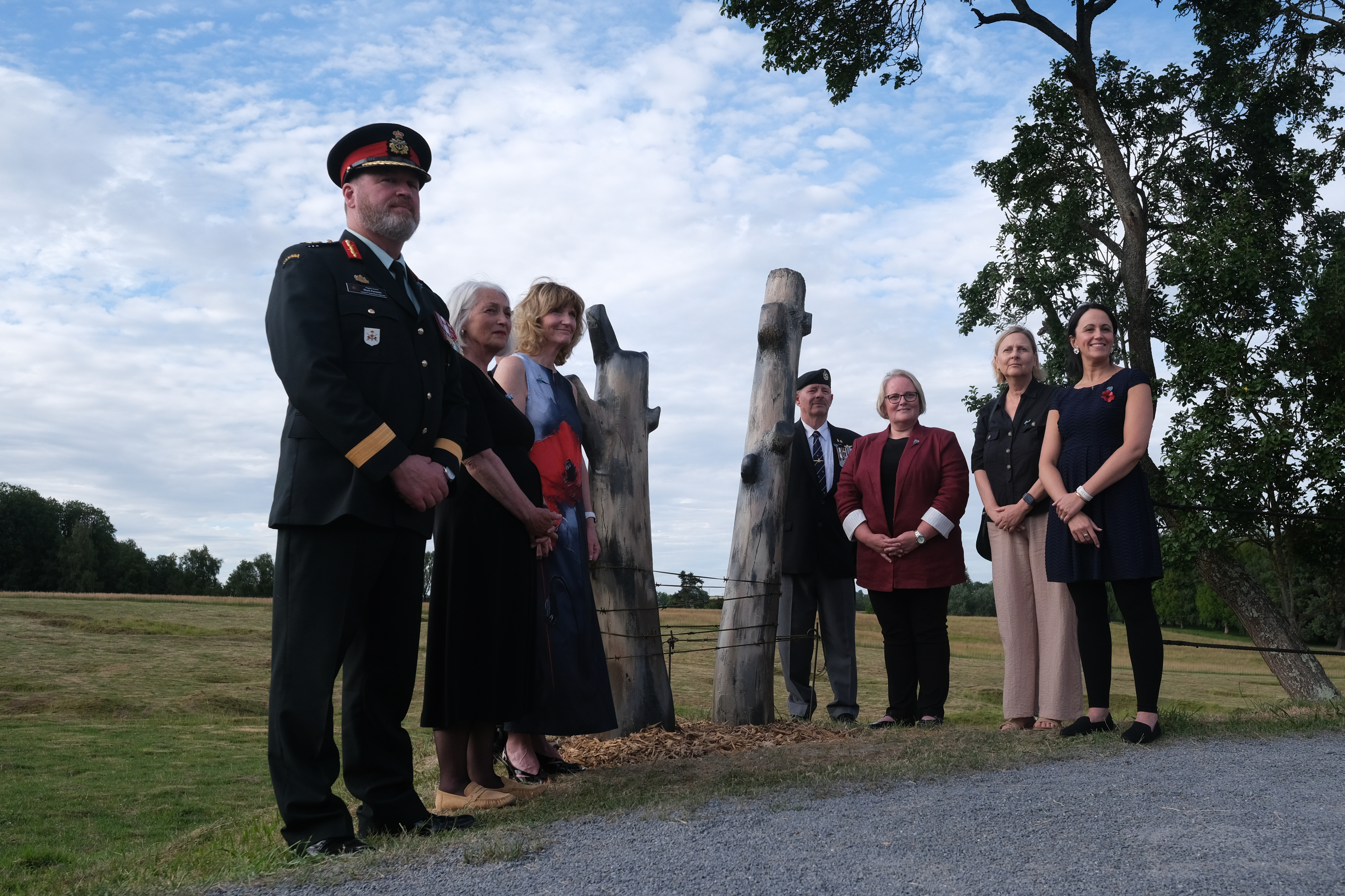 Seven adults stand outdoors beside a set of tall wooden posts in a grassy park.