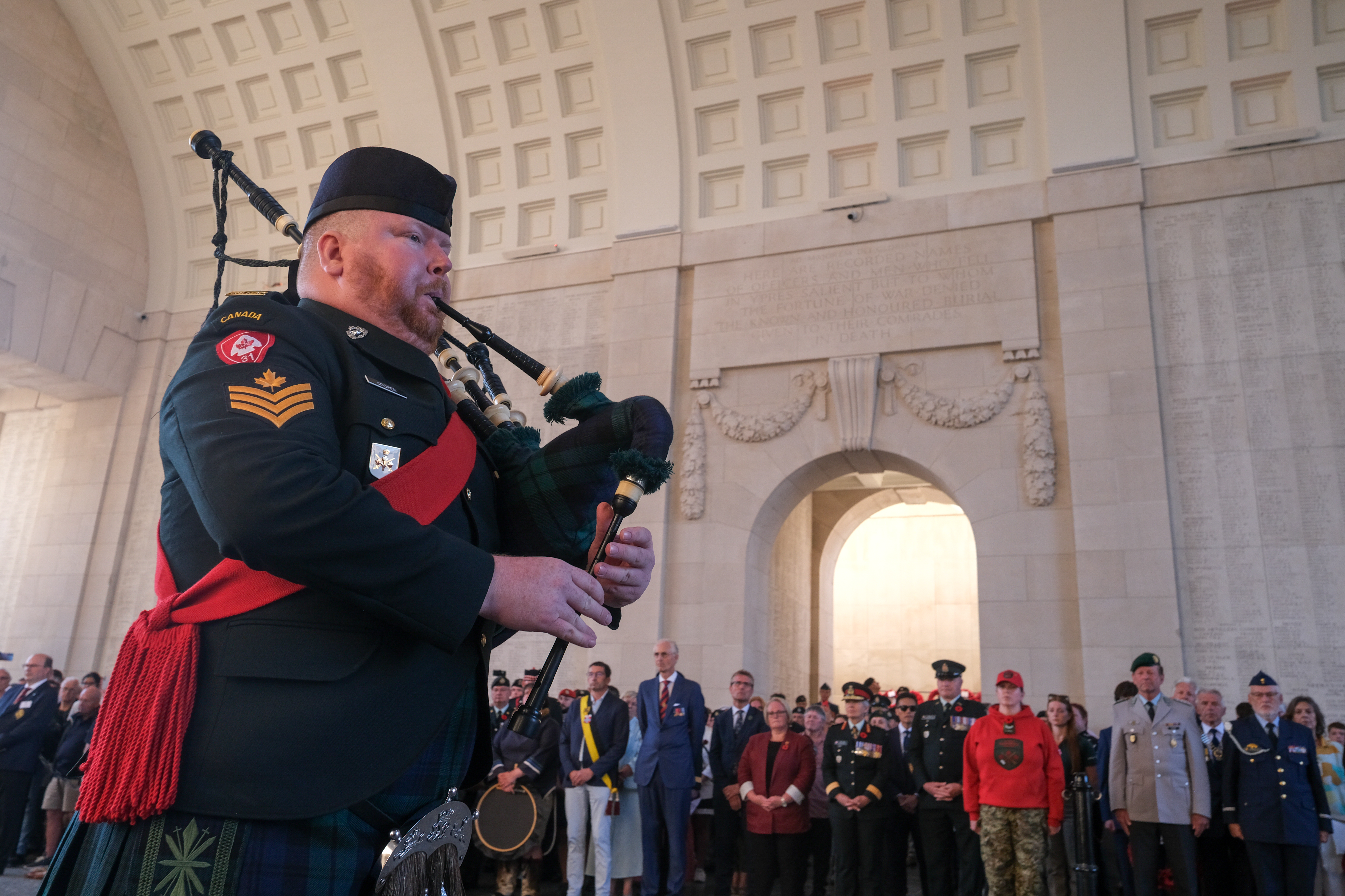 A person plays bagpipes inside a memorial hall while a group of attendees.