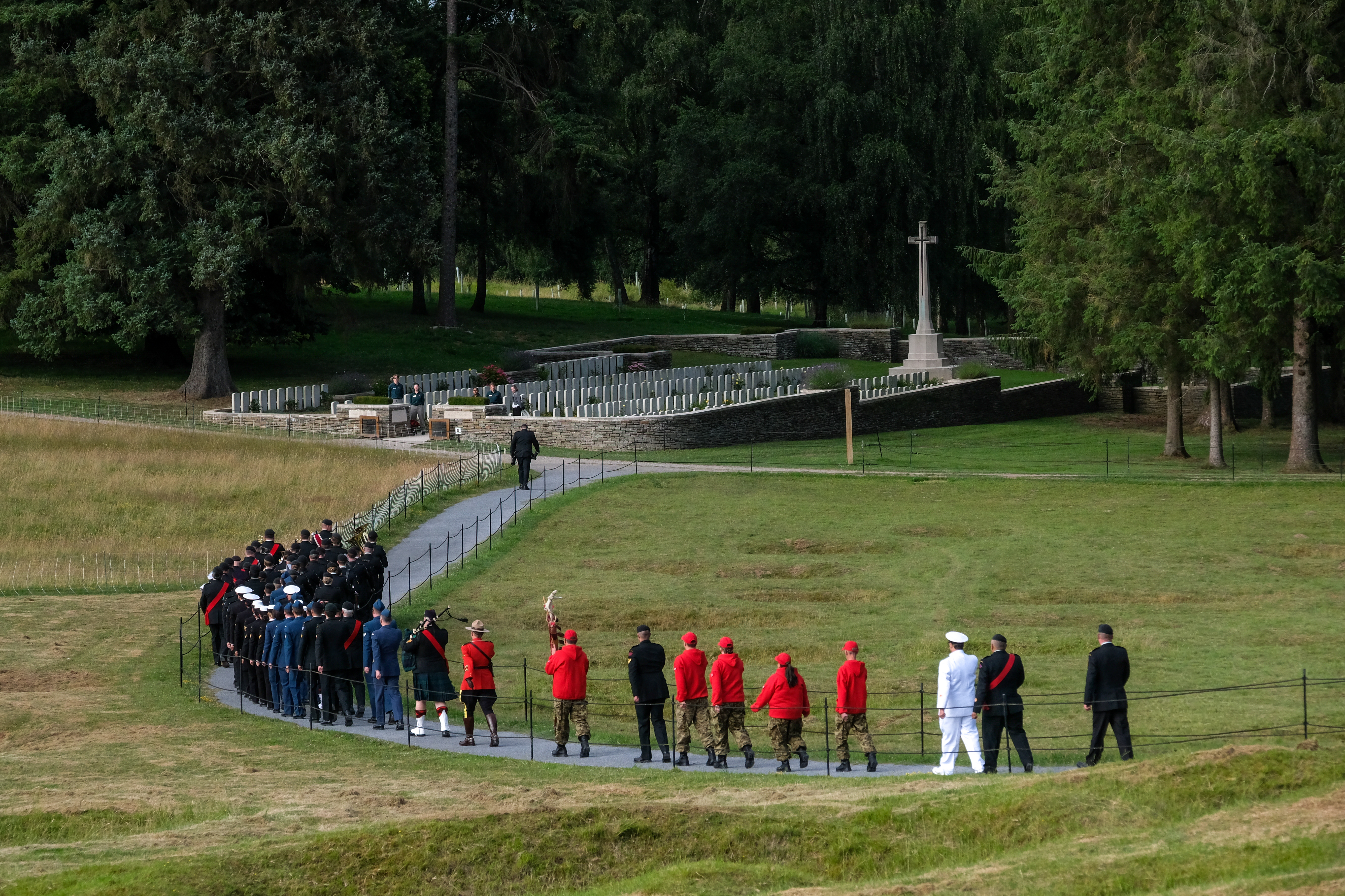 A group of people walk along a path toward a cemetery and memorial cross.