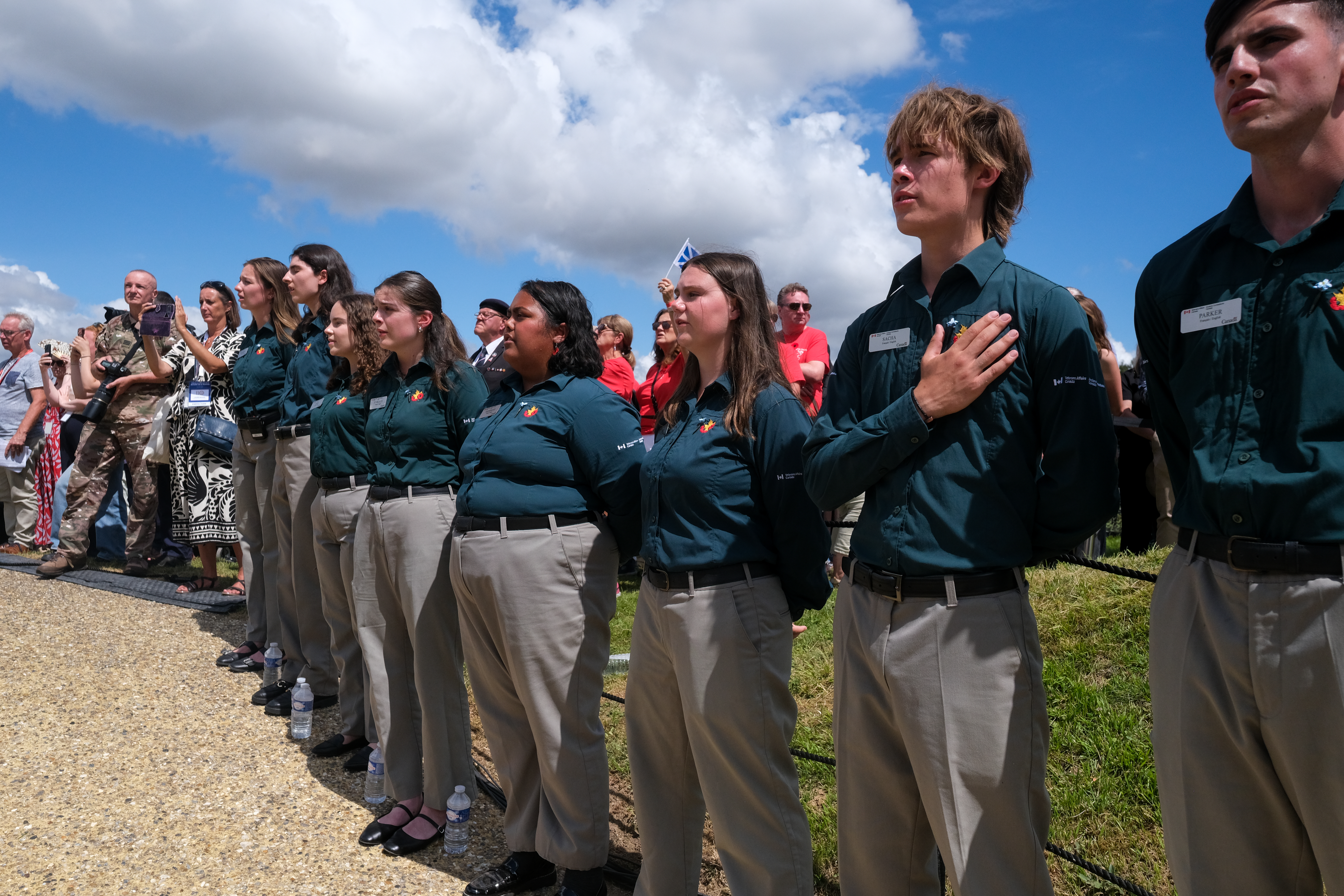 A group of young people stand outdoors with one hand over their heart.