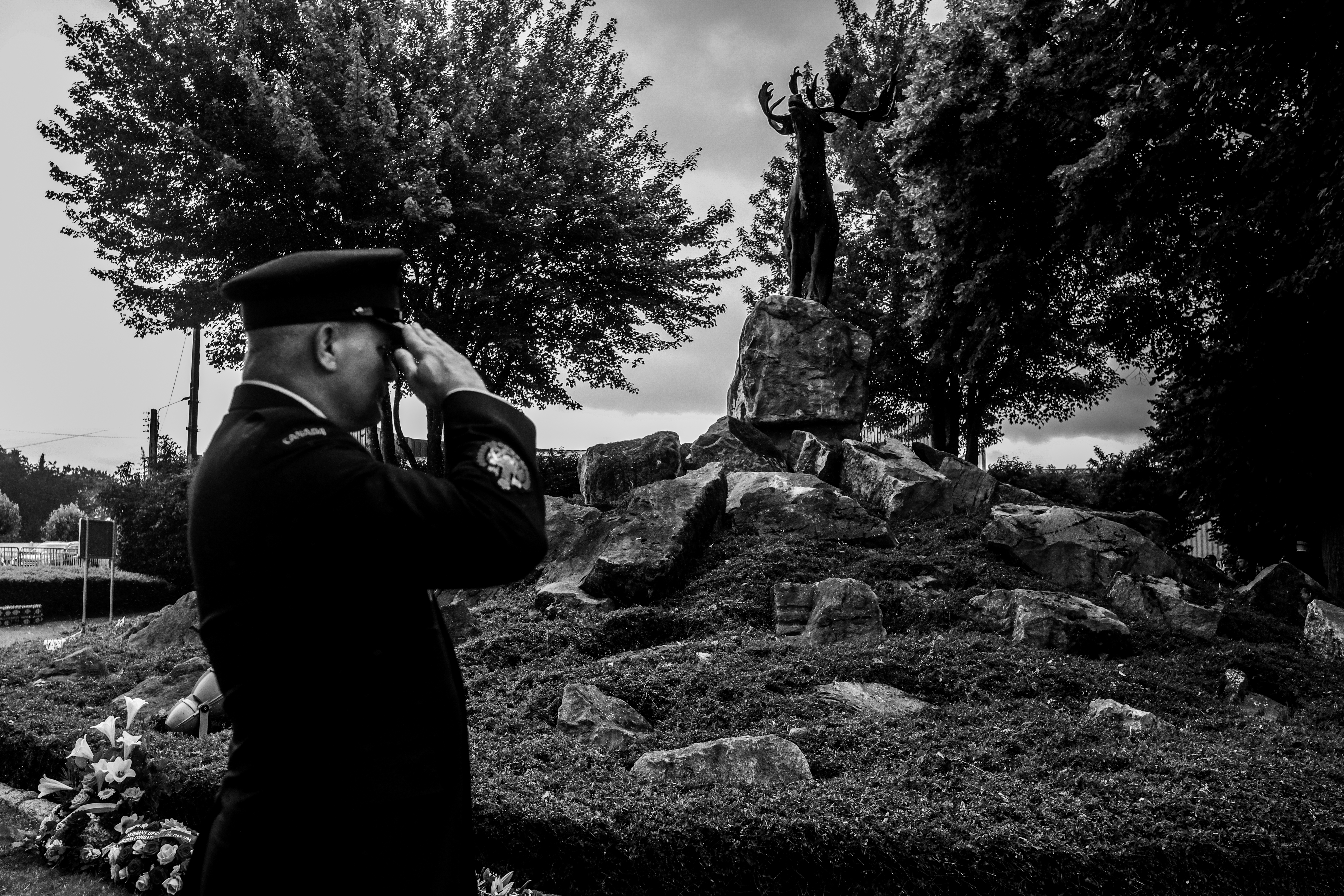 A uniformed person salutes near a memorial statue.