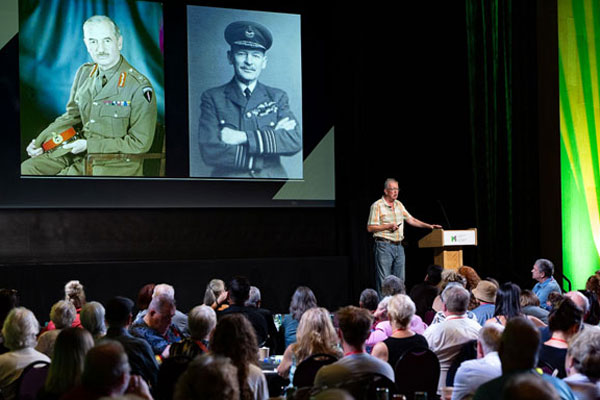 Un conférencier s’adresse à un public au Musée canadien de la guerre, tandis que deux grands portraits militaires historiques sont projetés sur un écran derrière lui.