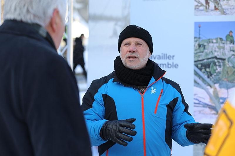 Dutil, wearing a blue winter jacket and black toque and black leather gloves stands outside speaking to a grey-haired man in a black coat.