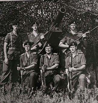 Une vieille photo en noir et blanc de six jeunes militaires lors d’un exercice d’instruction. Trois sont agenouillés, trois sont debout derrière, tous tiennent des fusils et sont vêtus d’uniformes militaires.
