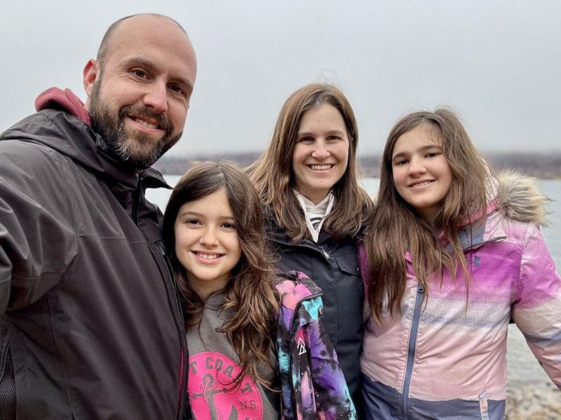 Bryan Martell with his wife and two daughters. They are outside in an overcast setting and are wearing jackets.