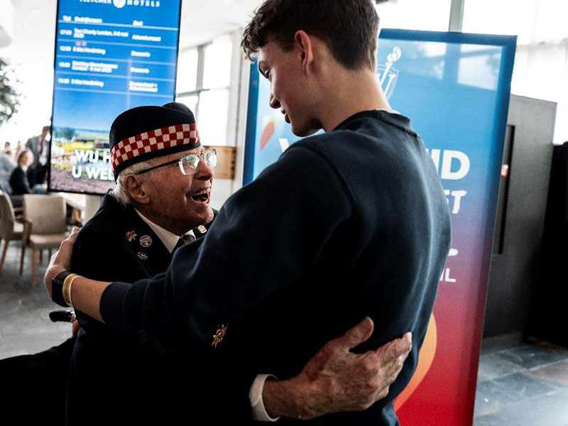 Lors d’un événement tenu à l’intérieur, un vétéran en uniforme échange une chaleureuse accolade avec un jeune.