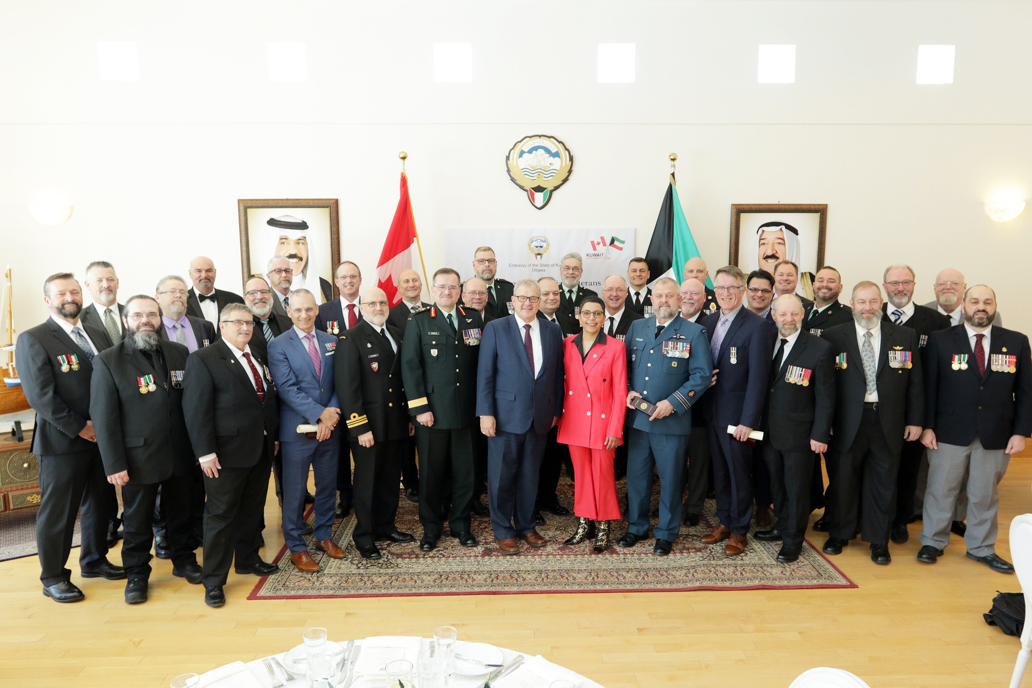 A group of people posing together for a photo with the flags of Canada and Kuwait behind them. 