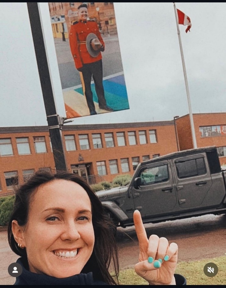 A woman stand smiling, pointing to a banner of a woman RCMP officer dressed in red serge.