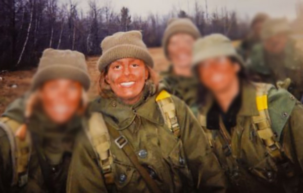 A group of four young women wearing military fatigues and hats pose smiling for a photo  
They have mud smeared on their faces.