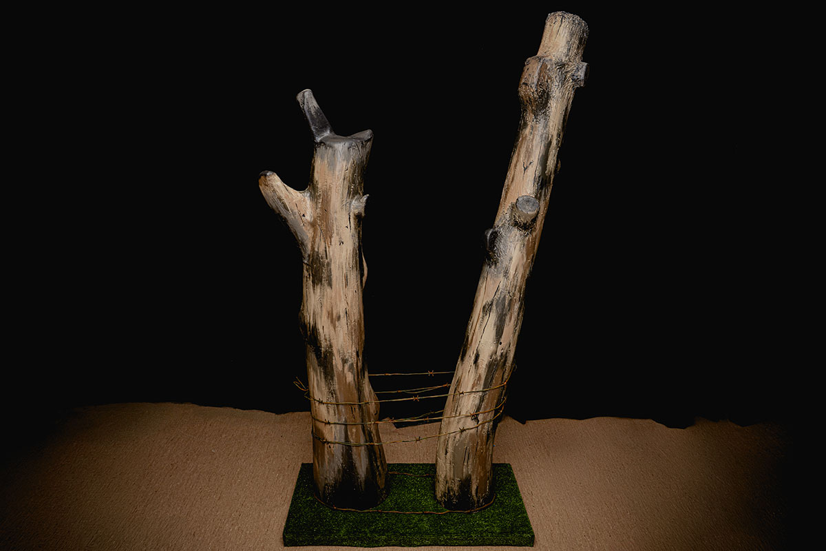 Une réplique de l’arbre du danger est exposée, représentant deux troncs endommagés joints et enveloppés de fil de fer à la base.