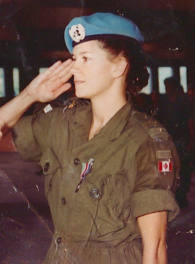 A young female soldier (Sandra Perron) salutes to someone off camera. She is wearing a Canadian military uniform and a blue beret on her head, signifying peacekeepers.