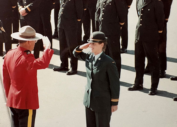 Sherry Lundrigan in a green military uniform saluting an officer in a red RCMP dress uniform. They are standing in front of a line of graduates.
