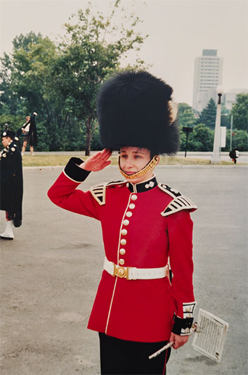 Shona Mitchell giving a salute. She is wearing a red ceremonial uniform and a black hat and is holding a flute in her hand.