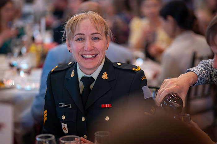 Photo 4: Shona Mitchell sitting at a dinner table with other groups of people around her. She is wearing a formal military uniform.