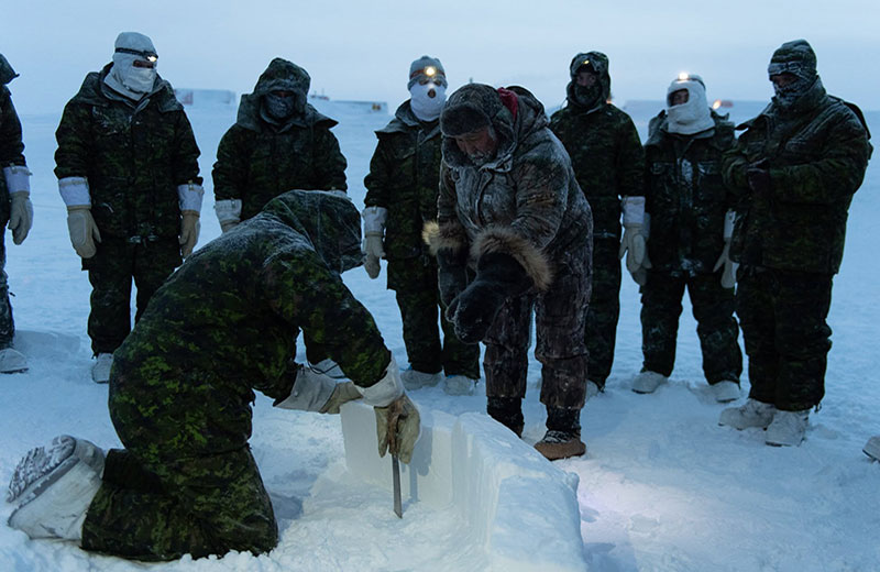 Solomon Awa working with a group of people to build an igloo in a field of snow and ice. Everyone is wearing thick winter clothing, and some are wearing headlamps.