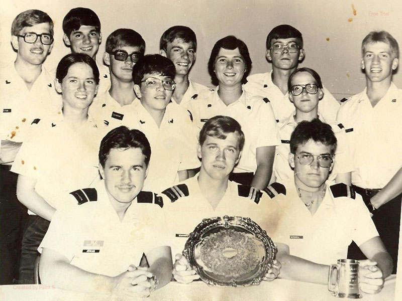 Steven Deschamps and 13 other young cadets pose for a photo. They are all wearing light coloured shirts with black epaulets on their shoulders. Steven is sitting in the front row, middle and is holding a silver platter.