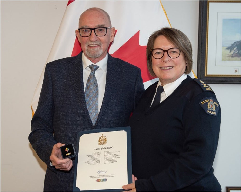 Gros plan du portrait officiel de Wayne Davis. Il sourit et ne regarde pas directement la caméra. Wayne a une moustache et porte un écusson official de la GRC attaché à son col. 